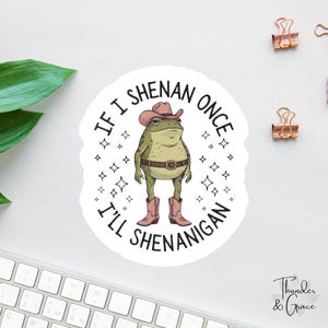 May include: A round sticker featuring a cartoon frog wearing a cowboy hat, belt, and boots. The text around the frog reads "If I Shenan Once, I'll Shenanigan." The sticker has a white background with star accents.