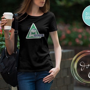 May include: A black t-shirt with a green triangle graphic featuring a white figure with a blue ring around it. The text "YOYODYNE" is printed on the graphic. The t-shirt is being worn by a person.