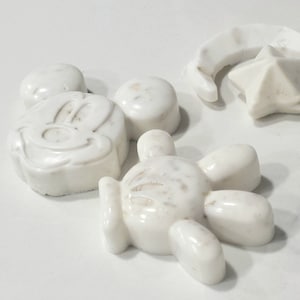 May include: Five white soap bars shaped like Mickey Mouse, a star, a crescent moon, and two Mickey Mouse hands. The soap bars have a textured surface.
