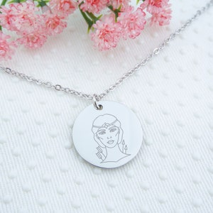 May include: A silver necklace with a round pendant featuring a line drawing of a woman with a crown and arrows.