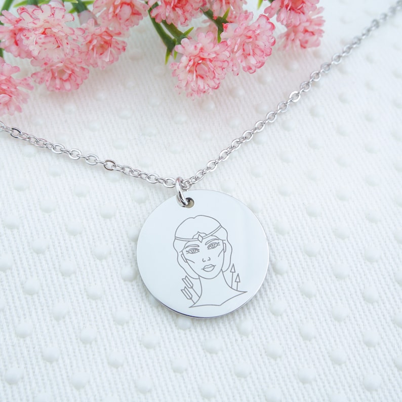 May include: A silver necklace with a round pendant featuring a line drawing of a woman with a crown and arrows.