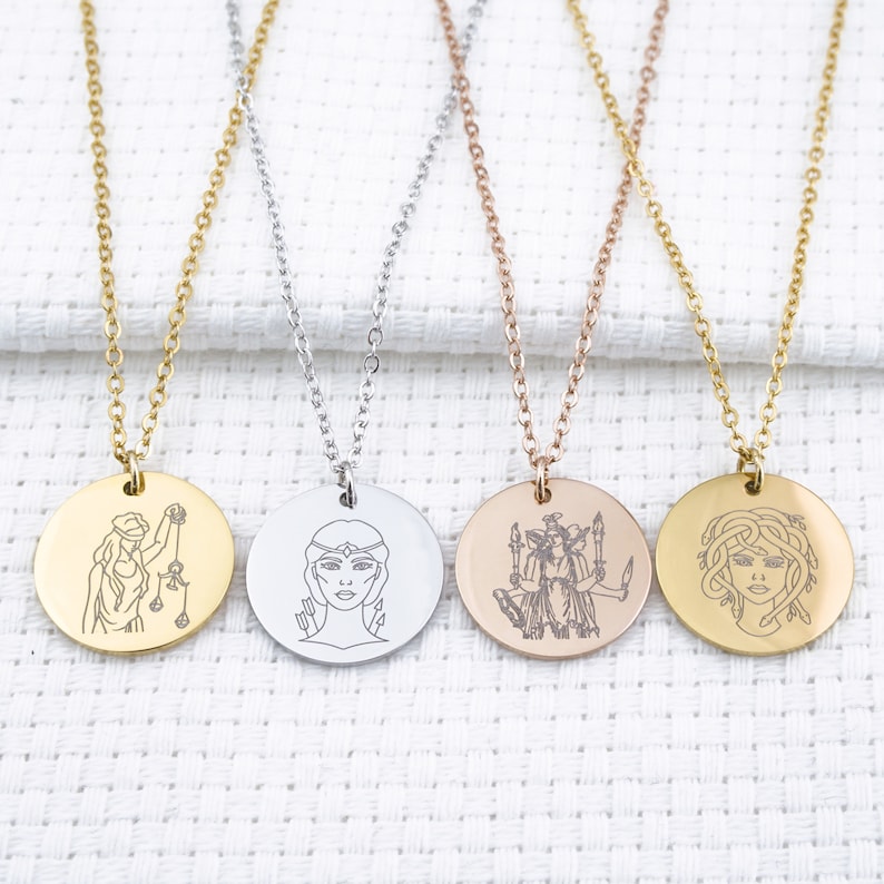 May include: Four silver necklaces with round pendants featuring different engraved images of women. The necklaces are on a white fabric background.