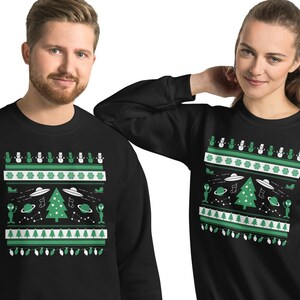 Könnte beinhalten: Schwarzes Sweatshirt mit einem grün-weißen Weihnachtsmotiv zum Thema Aliens. Das Design umfasst UFOs, Weihnachtsbäume, Aliens und Lichterketten. Das Sweatshirt wird von zwei Personen getragen.