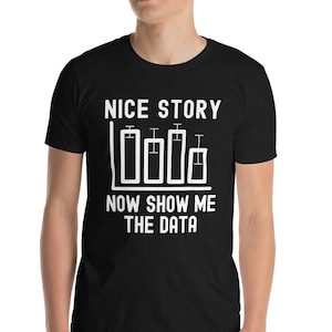 Puede incluir: Camiseta negra con texto blanco y un diseño de gráfico de barras. El texto dice "NICE STORY NOW SHOW ME THE DATA". La camiseta es de manga corta y está hecha de un material suave.