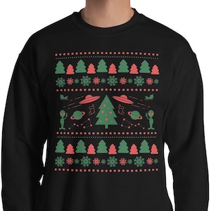 Könnte beinhalten: Schwarzes Sweatshirt mit einem festlichen Design mit grünen Weihnachtsbäumen, roten Schneeflocken und Elementen zum Thema Aliens. Das Design umfasst UFOs, Planeten und grüne Aliens.