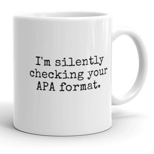 May include: White ceramic coffee mug with black text that reads "I'm silently checking your APA format."