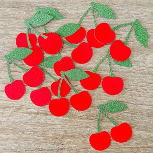 Op de afbeelding: Een verzameling rode papieren kersen met groene papieren bladeren. De kersen zijn uit papier geknipt en hebben een glanzende afwerking.