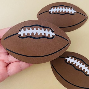 May include: Three brown paper footballs with white stitching. The footballs are cut out and have a black outline.