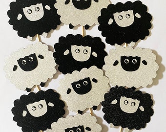 May include: Ten black and white sheep cake toppers with glitter. The sheep have black eyes and noses and are in various poses.
