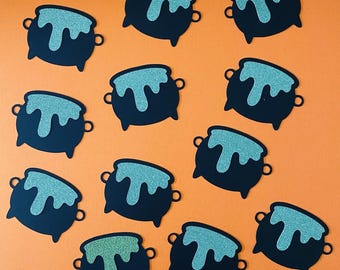 May include: A collection of black cauldron cutouts with teal glittery liquid spilling over the top. The cauldron shapes have small handles on each side and are arranged on an orange background. These are likely Halloween-themed decorations.