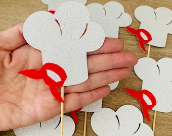 May include: Silver glitter chef hat cupcake toppers with red fabric band. The toppers are on wooden sticks.