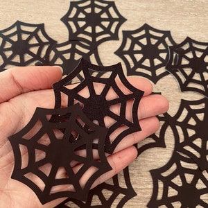 Op de afbeelding: Een verzameling zwarte papieren spinnenwebben, uitgeknipt in een delicaat ontwerp, perfect voor Halloween-decoraties.