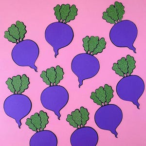 May include: A pattern of purple beet illustrations with green glittery tops on a pink background. The beets are stylized with a rounded body and a long, pointed tail. The green tops have a textured, glittery appearance.