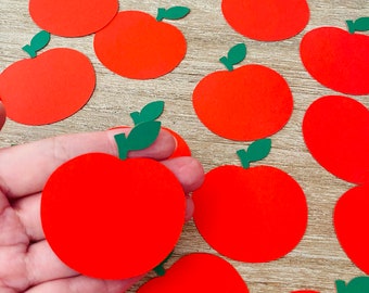 Puede incluir: Una colección de recortes de manzanas de papel rojo con tallos y hojas verdes. Las manzanas están dispuestas sobre una superficie de madera.