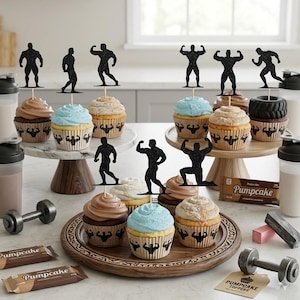 Puede incluir: Una colección de cupcakes con adornos de siluetas negras brillantes de culturistas en varias poses. Los moldes de los cupcakes están decorados con iconos negros de figuras musculosas. La presentación incluye barritas de proteínas y pesas.