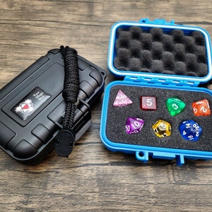 May include: A blue plastic case with a black latch and a black strap. The case is open and contains seven colorful dice. The dice are a variety of shapes and sizes, including a d4, d6, d8, d10, d12, and d20.