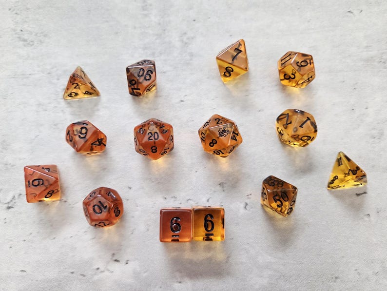 May include: A set of 11 amber dice with black numbers. The dice are in various shapes, including a d4, d6, d8, d10, d12, and d20.