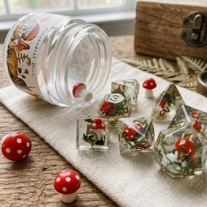 May include: A set of clear polyhedral dice containing miniature red and white mushrooms and green moss, with gold-colored numbers. The dice are spilled from a glass jar with a label reading Polyhedral Dice, accompanied by loose mushroom charms.