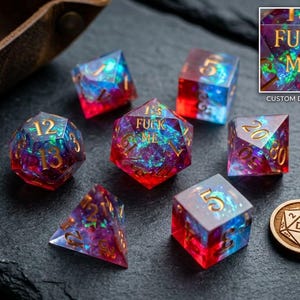 May include: A set of seven polyhedral dice made of translucent resin with a red and blue gradient, featuring iridescent foil flakes and gold-colored numbers. The central twenty-sided die displays the text FUCK ME in gold lettering.