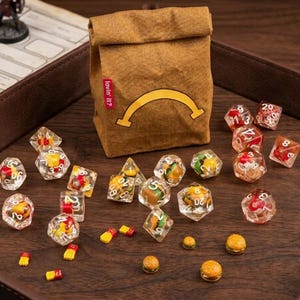 Peut inclure: Un sac en papier brun avec une ligne courbe jaune et le texte "lovin' it?" en rouge, entouré de dés polyédriques transparents contenant des breloques miniatures de burger et de frites, avec des petits morceaux de burger et de frites éparpillés.