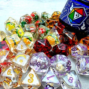 May include: A collection of polyhedral dice in various colors and designs, including clear, red, purple, and orange. Some dice have embedded objects, and others feature gold or white numbering. A blue container with a geometric design is visible.