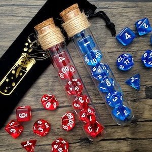 May include: Two glass test tubes filled with red and blue dice. The test tubes are wrapped in twine and have cork stoppers. The dice are scattered around the test tubes on a wooden surface.