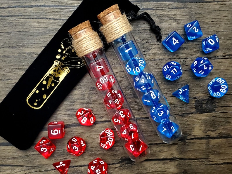 May include: Two glass test tubes filled with red and blue dice. The test tubes are wrapped in twine and have cork stoppers. The dice are scattered around the test tubes on a wooden surface.