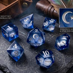 May include: A set of seven polyhedral dice labeled Night Sky Nebula Set, featuring deep blue translucent resin with white swirling nebula patterns and silver numbers. The D20 die displays a moon and star detail, with text reading Exquisite Moon & Star D20 Detail.