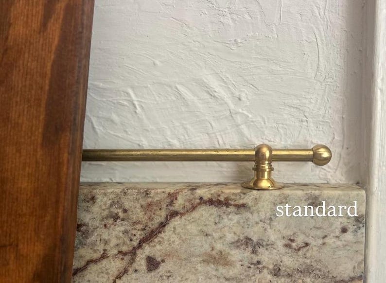 May include: A horizontal brass rod with a spherical end cap and a circular mounting bracket attached to a stone surface. The word standard is printed in white text on the lower right side of the image near the stone edge.