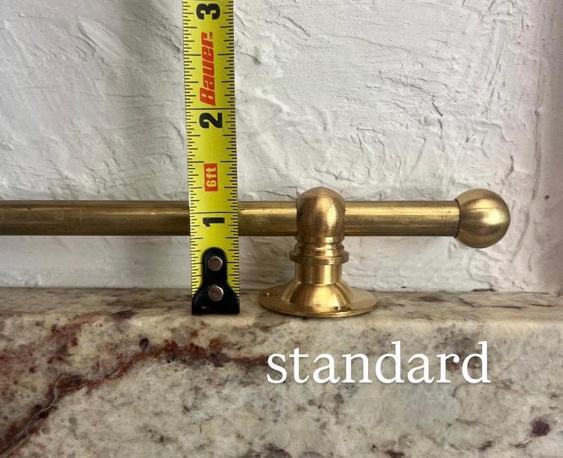 May include: A brass curtain rod with a spherical finial and a circular mounting bracket, positioned next to a yellow measuring tape showing a height of approximately 3.8 cm for the bracket. The word standard is printed below.