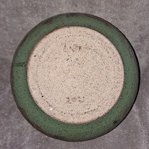 Puede incluir: Un posavasos de cer&aacute;mica hecho a mano con un centro moteado blanquecino y un borde verde. El borde tiene un aspecto envejecido y desgastado. La parte inferior del posavasos tiene el texto "4.29" y "2021".