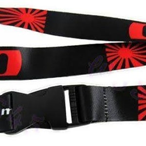 Könnte beinhalten: Schwarzes und rotes Lanyard mit einem weißen "NISMO"-Logo und einem roten aufgehenden Sonnenmotiv. Das Lanyard hat einen schwarzen Plastikclip und einen Metallschlüsselring.