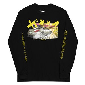 May include: Black long-sleeve t-shirt with a yellow graphic of a silver Nissan 350Z driving on a road with a sunset in the background. The Japanese text "ザ・オヤジ" is above the car and the text "CARTUNKS" is below the car. The text "ドリフトキング" is on the left sleeve and the text "キミガスキールサ" is on the right sleeve.