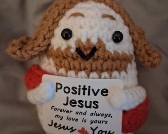 Puede incluir: Una pequeña figura redonda de ganchillo con hilo blanco para la cara y el cuerpo, hilo marrón para el pelo y la barba, y mangas rojas. Tiene ojos de plástico negro y sostiene una tarjeta blanca que dice: Positive Jesus, Forever and always, my love is yours, Jesus ❤️ You.