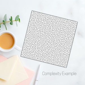 May include: A white square print featuring a complex black maze pattern. The text "Complexity Example" is printed in a light gray font at the bottom of the image. A cup of coffee, a pen, and an envelope are also visible.