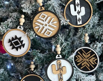 May include: A set of six round wooden ornaments with black and white geometric designs. The ornaments feature a snowflake, a cactus, a bull's head, and a geometric pattern. The ornaments are perfect for adding a touch of modern style to your Christmas tree.