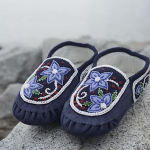 May include: A pair of blue moccasins with floral beadwork designs. The moccasins are made of soft leather and have a comfortable fit.
