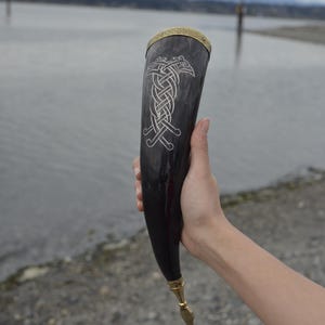 Può includere: Un corno da bere nero con un disegno in argento di due uccelli intrecciati. Il corno ha un bordo in ottone e una base in ottone.