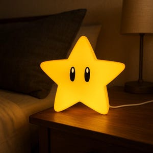 Peut inclure: Une veilleuse jaune en forme d'étoile avec des yeux ovales noirs. La lampe est branchée et posée sur une table de chevet en bois. L'arrière-plan comprend un lit et une lampe.