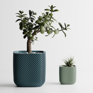 Puede incluir: Dos macetas decorativas, una grande y otra pequeña, cada una con una planta. La maceta más grande es de color verde azulado con un diseño texturizado y arremolinado. La maceta más pequeña es verde claro.