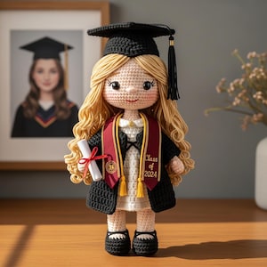 Puede incluir: Muñeca de ganchillo hecha a mano con birrete, toga y banda de graduación. La muñeca tiene cabello rubio y sostiene un diploma atado con una cinta roja. La banda dice "Class of 2024".