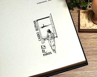 May include: Black and white illustration of a woman looking out a window at a lighthouse in the distance. The text "CANDIDO GUZMAN" is written vertically on the left side of the image. The text "EX LIBRIS" is written below the window.