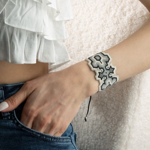 May include: A white and black beaded bracelet with a geometric pattern. The bracelet is tied with a black cord.