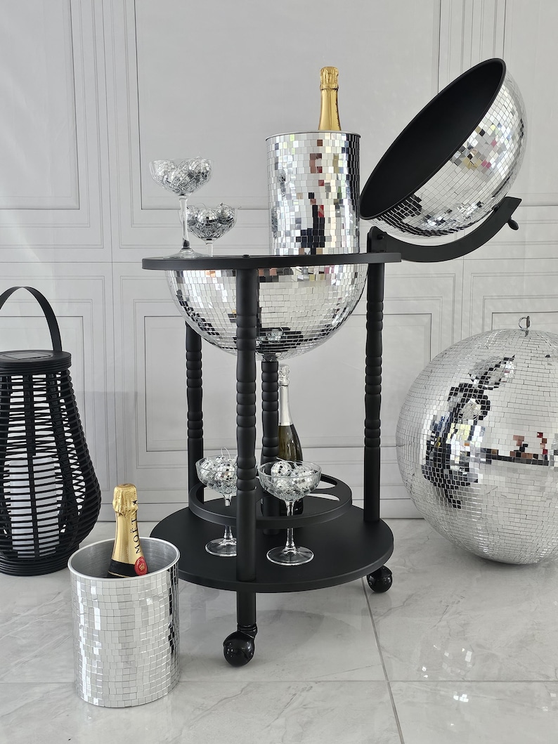 May include: A black drinks trolley with a mirrored disco ball design. It features champagne bottles, glasses, and a disco ball ice bucket. A black woven lantern and a large disco ball are also present.