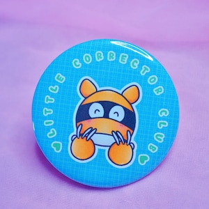 May include: A blue and white button featuring a cartoon tiger wearing a black mask. The text "Little Corrector Club" is written around the tiger in a green circle.