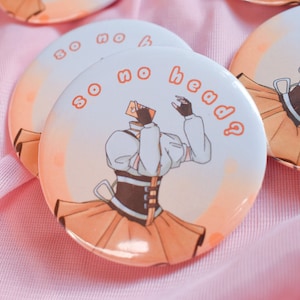 以下が含まれることがあります： 「so no head?」と書かれたカードを持った、頭のない人の漫画イラストが描かれた丸いボタン。その人は白いシャツ、茶色のコルセット、黄色のスカートを着ています。ボタンはピンクの表面にあります。