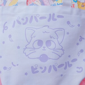 Puede incluir: Bolsa de lona blanca con un dise&ntilde;o de gato de dibujos animados morado y el texto "ビッハイル" en caracteres japoneses. La bolsa tiene un patr&oacute;n de estrellas moradas.