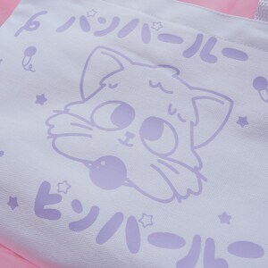 Puede incluir: Bolsa de lona blanca con un dise&ntilde;o de gato de dibujos animados morado. El gato sostiene una pelota morada. El texto "パジャマール" est&aacute; impreso en morado en la bolsa.