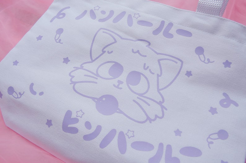 Puede incluir: Bolsa de lona blanca con un dise&ntilde;o de gato de dibujos animados morado. El gato sostiene una pelota morada. El texto "パジャマール" est&aacute; impreso en morado en la bolsa.