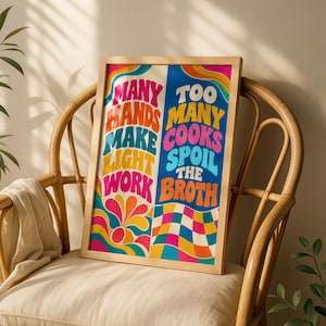 May include: A rectangular framed wall art print featuring a split design with colourful, wavy typography. The left side reads Many Hands Make Light Work in red, orange, and blue, while the right side reads Too Many Cooks Spoil The Broth.